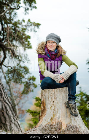 Frau Winter Kleidung sitzt auf einem Baumstumpf Stockfoto
