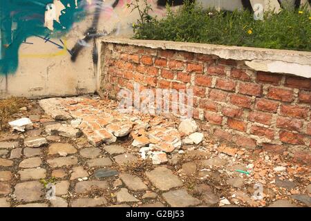 Niedrige Auflösung der alten gemauerten Wand. Ziegel auf einer asphaltierten Straße liegen. An der Wand ist sichtbar graffiti Stockfoto