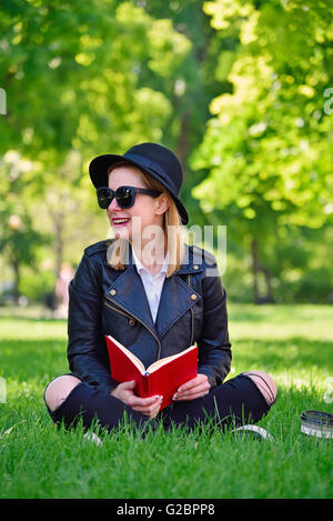 Hipster Mädchen mit Hut sitzen auf Rasen mit Buch Stockfoto