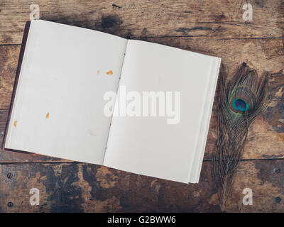 Eine offene Notebook und einer Pfauenfeder auf einem Schreibtisch aus Holz Stockfoto