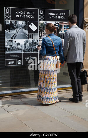 Passanten betrachten Anzeige historischer Bilder der Stadt. Mai Spring Bank Holiday in Manchester Central Business District Anzeige von alten Fotos, Foto, retro, Vintage, Hintergrund, Fotografie, Kamera, Bild, weiß, Rahmen, Classic, Illustration, abstrakt, Holz, Nostalgie, feiern die Vergangenheit, die Gegenwart und die Zukunft der King Street. Stockfoto