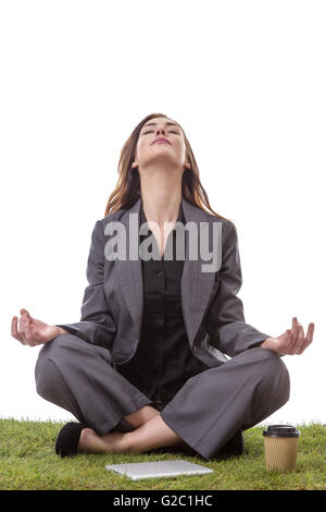 Hübsche junge Geschäftsfrau in einem Anzug, sitzen auf dem Rasen in einem gekreuzten Beinen Yoga-Pose, mit ihre Arme ruhen auf den Knien, Palmen u Stockfoto