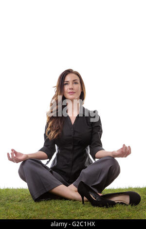 Hübsche junge Geschäftsfrau in einem Anzug, sitzen auf dem Rasen in einem gekreuzten Beinen Yoga-Pose, mit ihre Arme ruhen auf den Knien, Palmen u Stockfoto