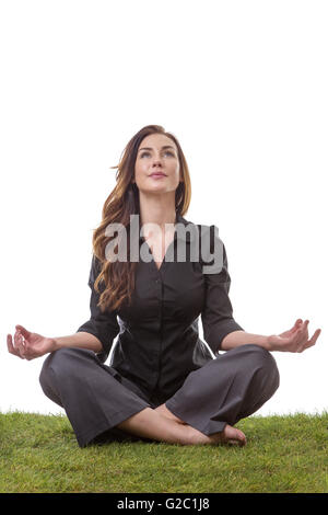 Hübsche junge Geschäftsfrau in einem Anzug, sitzen auf dem Rasen in einem gekreuzten Beinen Yoga-Pose, mit ihre Arme ruhen auf den Knien, Palmen u Stockfoto