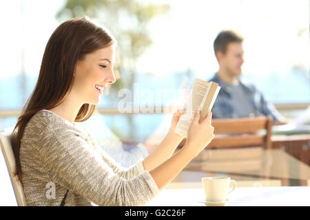 Glückliche Frau ein Buch Papier in einem Café an einem sonnigen Tag mit Menschen sitzen im Freien im Hintergrund Stockfoto