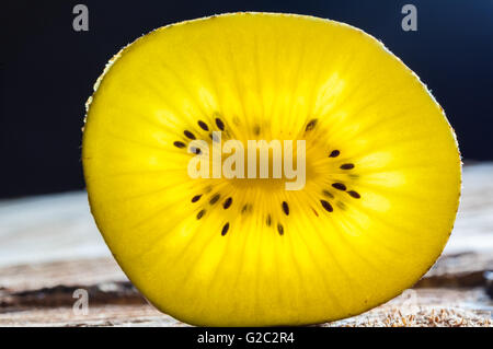 Nahaufnahme des gelben Kiwi-Scheibe mit durchscheinenden Licht auf rauen Holzoberfläche Glühen Stockfoto