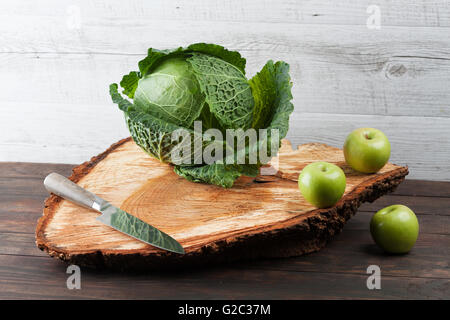 Ganze Kohl mit drei grünen Äpfeln und Küchenmesser auf groben hölzernen Schneidebrett mit Textfreiraum Stockfoto