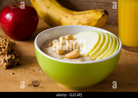 Haferflocken-Porridge mit Äpfeln, Zimt, Nüssen und Goji-Beeren. Müsliriegel, frisches Obst und Orangensaft auf hölzernen Hintergrund Stockfoto