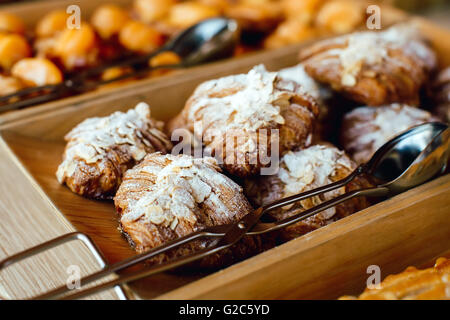 Croissants, bestreut mit Mandeln und Puderzucker in ein Holztablett mit Metall Zange Stockfoto