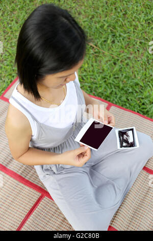 Asiatische-schwangere Frauen zeigen Ultraschallbild Film Baby auf den Bauch in der hand im Garten. Stockfoto