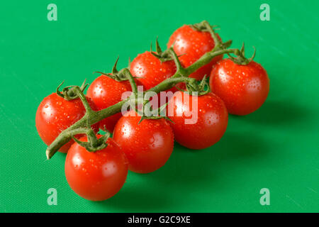 Tomaten an den Rebstöcken gezeigt auf einer grünen Schneidebrett, die richtige Farbe für Lebensmittelhygiene Stockfoto