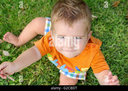 Blondes Baby sitzen auf dem Rasen mit einem Zweig in seiner Hand-Draufsicht Stockfoto