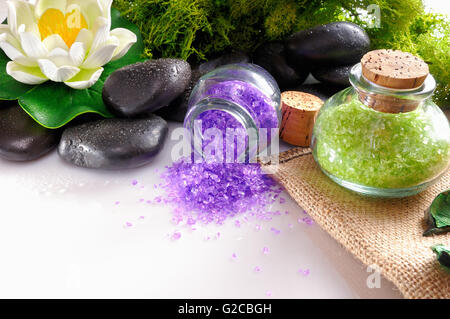 Badesalz hautnah mit schwarzen Steinen und Moos Blume Glas auf weißen Tisch. Horizontale Komposition Stockfoto