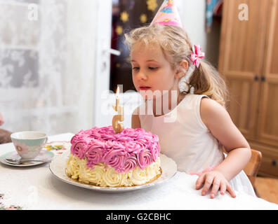 Porträt von hübschen Mädchen mit 5-Jahres-Geburtstagstorte, sitzen am Tisch und machen einen Wunsch Stockfoto