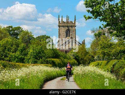 Ein Radfahrer entlang einer Landstraße tragen Schlachtfeld Kirche in Shropshire, England, UK. Stockfoto