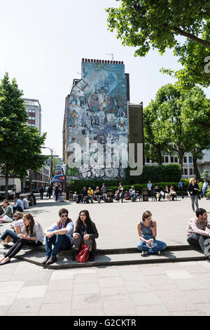 Menschen entspannen vor ein Wandgemälde an der Seite eines Gebäudes in Tottenham Court Road, London, UK Stockfoto