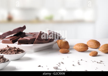 Portionen und Schokoladenstückchen mit Mandeln auf einem weißem Porzellan Behälter auf einem weißen Tisch in der Küche. Horizontale Komposition. Stockfoto