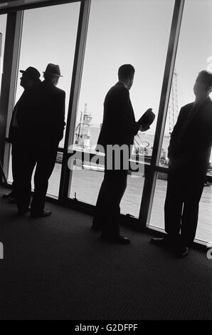 Silhouette von vier Männern in Anzügen in der Nähe von großen Fenster mit Booten im Hintergrund Stockfoto