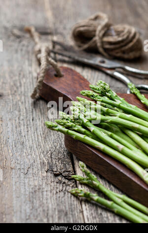 Frischer Spargel auf ein Schneidebrett, Schere, Faden auf den alten hölzernen Hintergrund Stockfoto