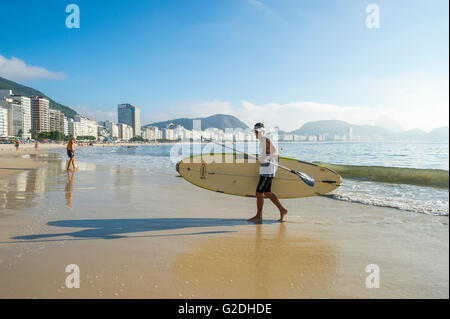 RIO DE JANEIRO - 5. April 2016: Ein Junge brasilianische Mann trägt einen Stand up Paddel Longboard Surfbrett am Strand Copacabana. Stockfoto