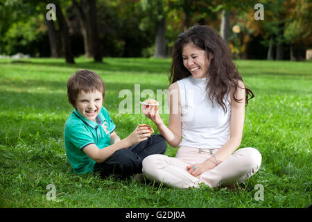 Kid Boy und Frau Spaß Essen einen Muffin im Park sitzen auf dem Rasen im park Stockfoto