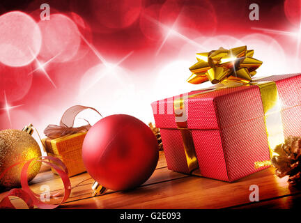 Rot Weihnachten Dekoration auf einer Tabelle Holzlatten. Mit Geschenk-Boxen, Kugeln, Band und Tannenzapfen. Mit roten Bokeh Hintergrund mit Stockfoto