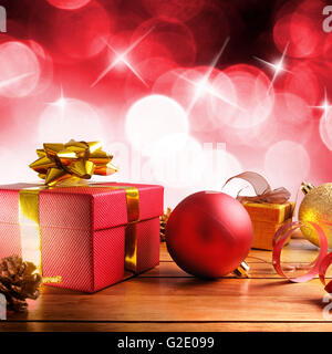 Rot Weihnachten Dekoration auf einer Tabelle Holzlatten. Mit Geschenk-Boxen, Kugeln, Band und Tannenzapfen. Mit roten Bokeh Hintergrund mit Stockfoto
