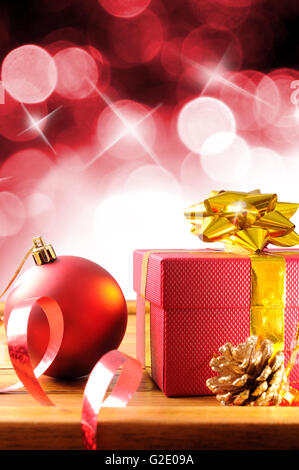 Rot Weihnachten Dekoration auf einer Tabelle Holzlatten. Mit Geschenk-Boxen, Kugeln, Band und Tannenzapfen. Mit roten Bokeh Hintergrund Stockfoto