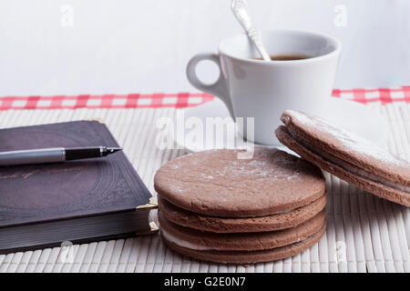 Große Runde, braune Kekse mit alten Notebook und Füllhalter mit Kaffeetasse im Hintergrund Stockfoto