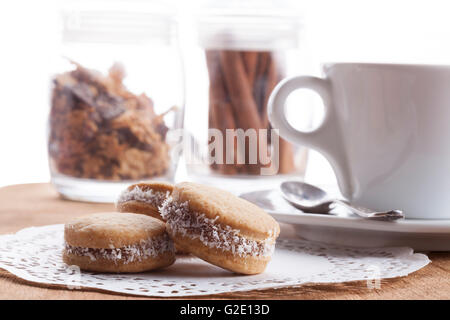 Kleine Runde Cocnut Cookies mit weißen Kaffeetasse in der Bakcground auf Holzplatte Stockfoto