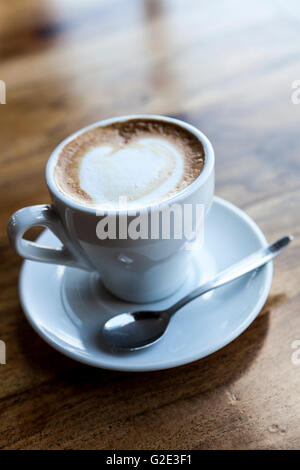 Cappuccino in weiße Tasse mit Teller und Löffel auf Holztisch Stockfoto