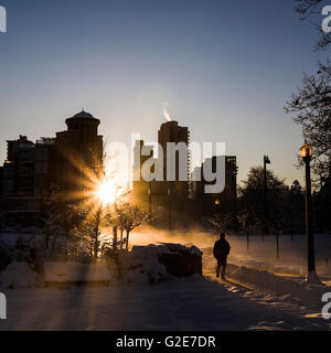 Mann zu Fuß durch verschneiten Stadtpark mit Sonne durch Stadtbild, Vancouver, Kanada Stockfoto