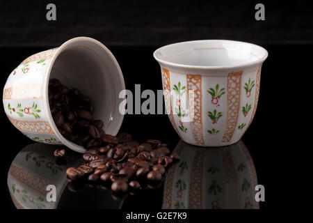 Handgemalte traditioneller arabischer Kaffeetassen auf schwarzem Hintergrund und Kaffeebohnen mit Reflexion Stockfoto