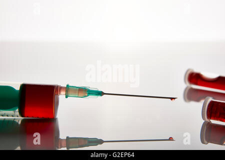 Spritze und Fläschchen mit Blutabnahme über weißem Glastisch. Horizontale Komposition. Ansicht von vorne. Stockfoto