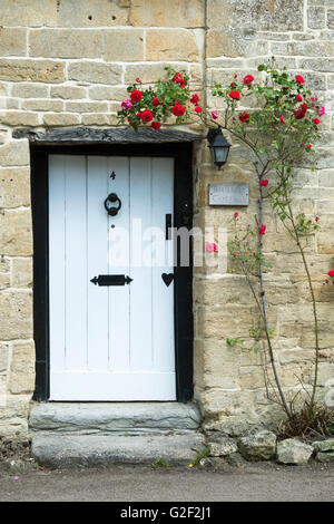 Cotswold Landhaus aus Stein mit roten Rosen um vor die Haustür. Stanton, Cotswolds, Gloucestershire, England Stockfoto