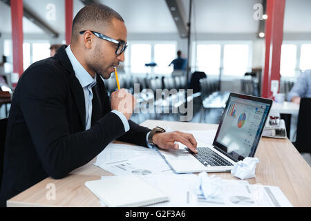 Jungen Geschäftsmann Blick auf seinem Laptop sitzend an seinem Arbeitsplatz im Büro konzentriert Stockfoto