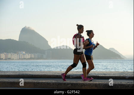 RIO DE JANEIRO - 3. April 2016: Ein paar Jogger auf der Copacabana Promenade pass vor eine Zuckerhut Silhouette. Stockfoto