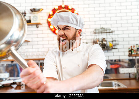 Crazy verrückt Chef-Koch mit Pfanne auf dem Küchentisch zu drohen Stockfoto