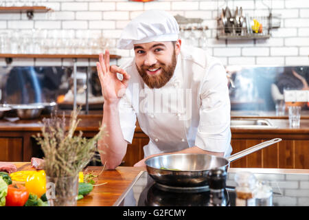 Fröhliche bärtigen Chef-Koch Kochen und ok Anzeichen auf die Küche Stockfoto