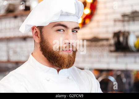 Nahaufnahme des schönen Lächelns bärtigen Chef-Koch in weißen Hut und Uniform auf dem Küchentisch Stockfoto