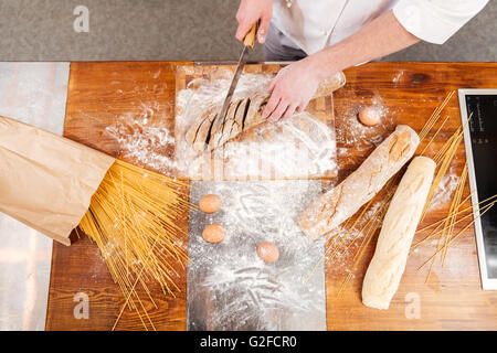 Draufsicht der Mann Bäcker stehen und das Schneiden von Brot an die Küche Stockfoto