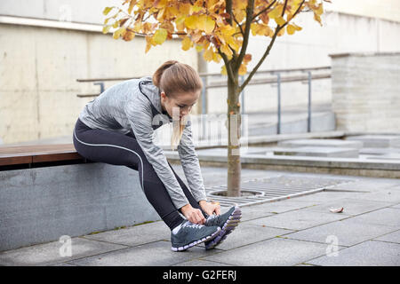 glückliche junge sportliche Frau binden Schnürsenkel im freien Stockfoto