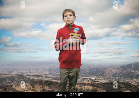 Kleiner Junge hält ausgestopfte Puppe gegen Berglandschaft Stockfoto