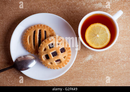 Tasse Tee und Zitrone, Kekse mit Marmelade in Untertasse Tabelle Draufsicht Stockfoto