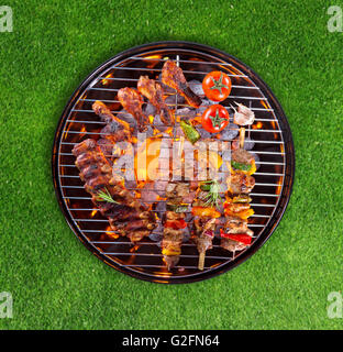 Schweinerippchen, Hähnchenschenkel, Spieße und Gemüse serviert auf Grill, grünen Rasen auf Hintergrund Stockfoto