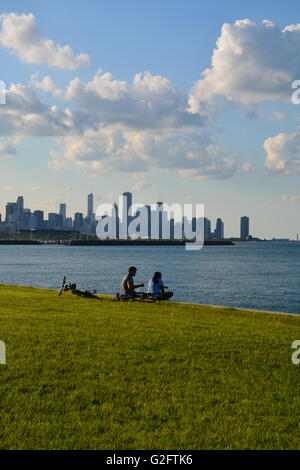 Ein Paar macht eine Pause auf dem Fahrradweg am See auf Chicagos Südseite des Kenwood-Viertels mit der Skyline der Stadt im Hintergrund. Stockfoto