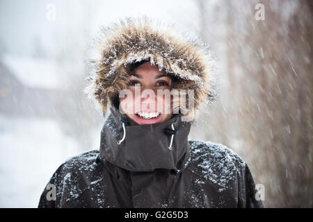Lächelnde junge Frau tragen Wintermantel im Schnee Stockfoto