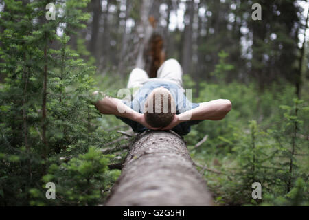 Junger Mann Verlegung auf Log in Wald Stockfoto