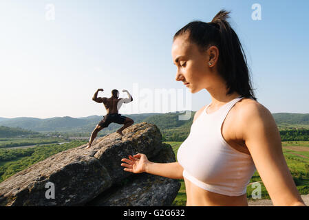 Gemischte Rassen paar kaukasischen Brünette Frau und afroamerikanische Mann mit muskulösen Körper gemeinsam Yoga zu praktizieren. Rocky Mountains-Hintergrund Stockfoto