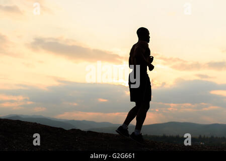 Silhouette des afrikanischen amerikanischen Sportler Joggen am Sonnenuntergang in Bergen Stockfoto